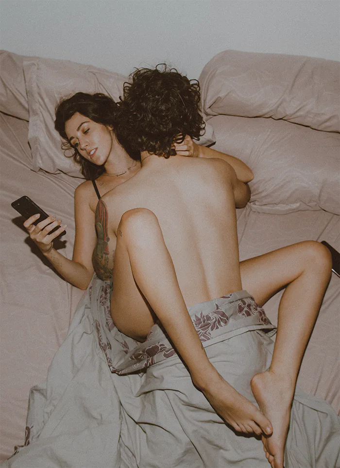 Para uprawiająca miłość, przykryta kocem. Kobieta przegląda ogłoszenia towarzyskie na telefonie.